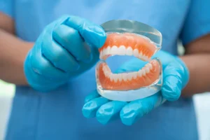 Dental professional wearing blue gloves holds a set of dentures at the Montana Center for Implants and Dentures, showcasing high-quality dental care and treatment options.