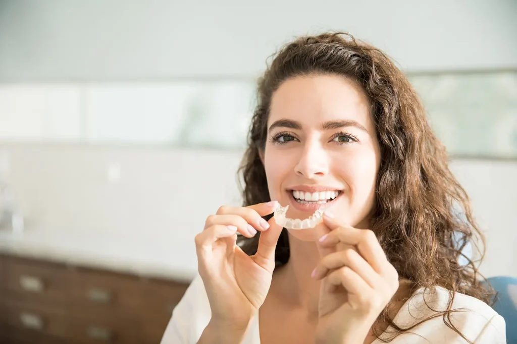 7 Painful Ways Teeth Grinding Impacts Your Oral Health 2 A patient at Montana Center for Implants and Dentures holding an orthodontic retainer to prevent teeth grinding and protect oral health.