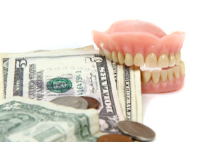 Dentures placed on U.S. dollar bills and coins, representing affordable treatment options from Montana Center for Implants and Dentures, including cheap options for missing teeth like dental implants and premium dentures.