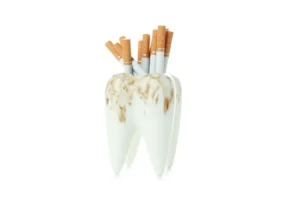 Tooth stained by tobacco holding cigarettes, illustrating risks related to the question can I smoke with dental implants, for Montana Center for Implants and Dentures.