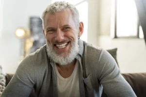 Smiling man with healthy teeth at home after long-lasting dental implants from Montana Center for Implants and Dentures answering the question how long do dental implants last