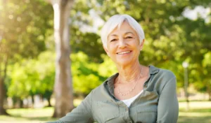 Senior woman smiling confidently in the park after getting dental implants for seniors.