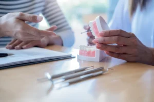 Dentist explaining dental implant aftercare to a patient using a denture model at Montana Center for Implants and Dentures.
