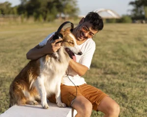 Young man in his 30s smiling with his dog while wearing headphones, showing confidence after getting dental implants for younger adults.